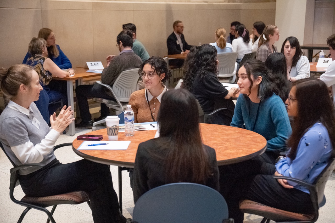 A woman speaking at a round table with four female students
