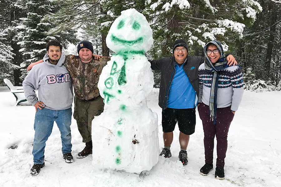 Julio Hernandez with three other Beta Theta Pi fraternity members standing with a large snowman they built. Beta Theta Pi is painted on the snowman's body.