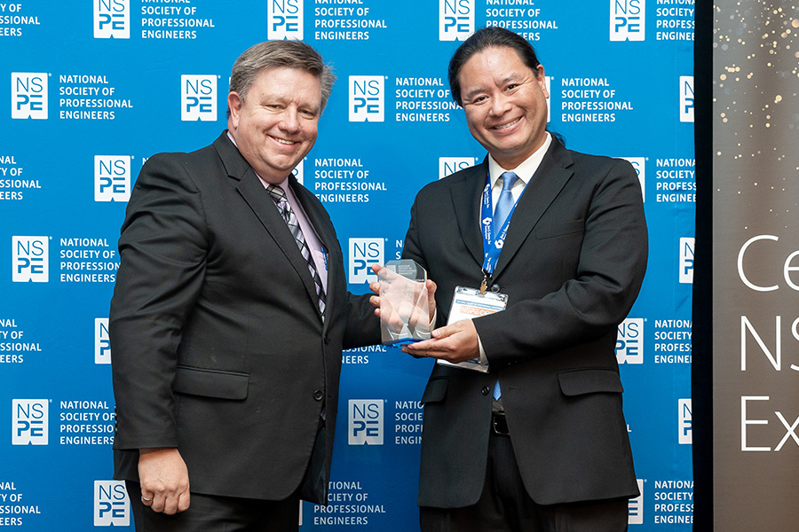 NSPE president Britt Smith handing a small glass trophy to Waterloo Tsutsui at NSPECon 2023