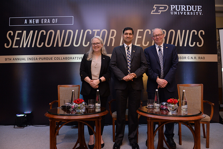 Heidi Arola, Vijay Raghunathan and Mark Lundstrom stand in front of a purdue branded backdrop, there are tables with bottles of water in the foreground, all are smiling