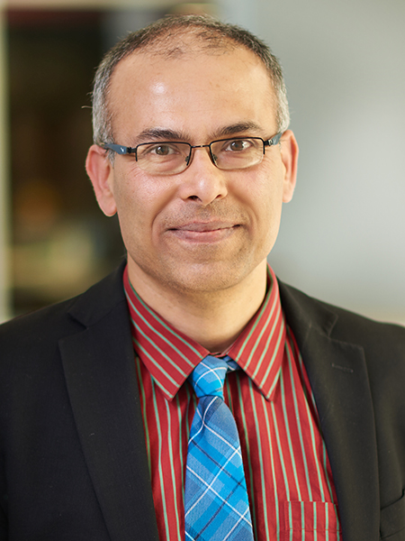 Portrait of Saurabh Bagchi. He is wearing a red shit, blue tie, and black suit jacket. The background is the atrium of the MSEE building.