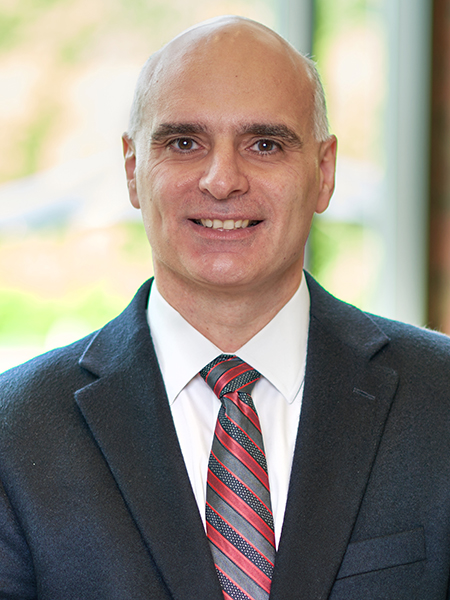 Portrait of Dimitrios Peroulis. He is wearing a black suit, white shirt, and patterned tie. This photo was taken in the atrium of the MSEE building.