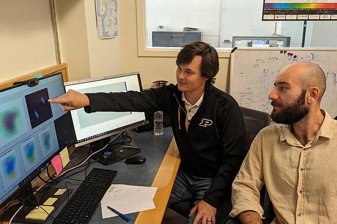 Colton Fruhling, postdoctoral researcher (left), and Mustafa Goksu Ozlu, graduate research assistant in Purdue Universitys Elmore Family School of Electrical and Computer Engineering, are seated at a desk with multiple computer monitors that are displaying technical renderings.