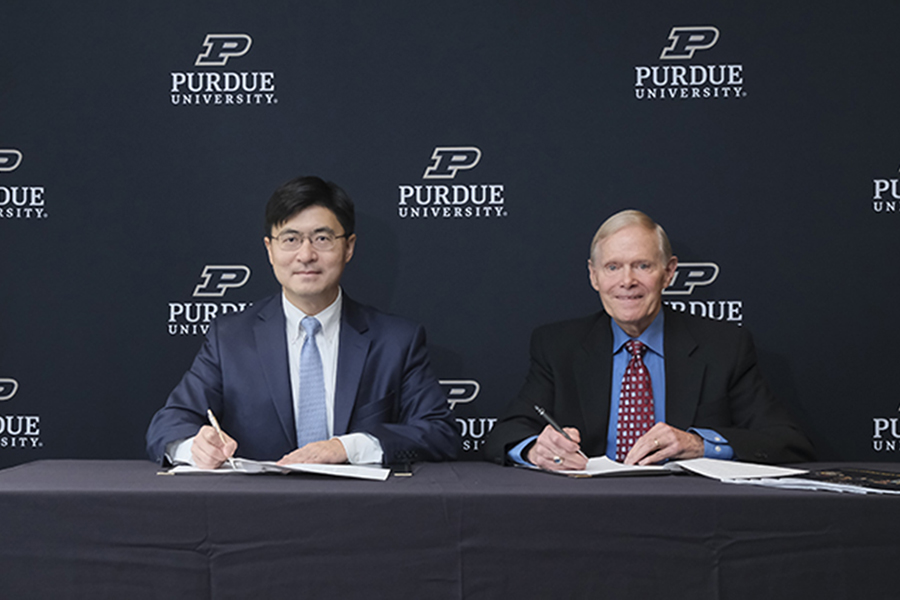 Purdue President Mung Chiang sits to the left of the Rick Cassidy, chairman of TSMC Arizona, in front of Purdue University backdrop.