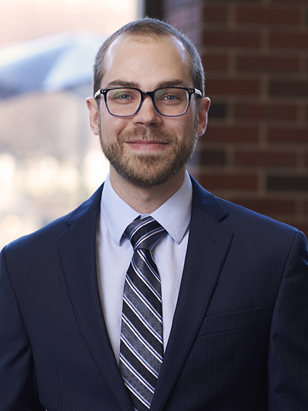 This is a portrait of Professor Thomas Roth. He has short cut hair along with a closely shaved beard. He is wearing glasses and suit with tie.