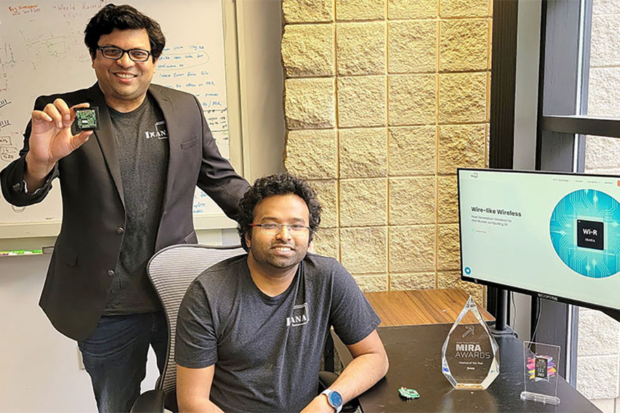 Professor Shreyas Sen is standing behind alumnus Shovan Maity. Sen is holding a silicon chip while Maity is seated at a computer.