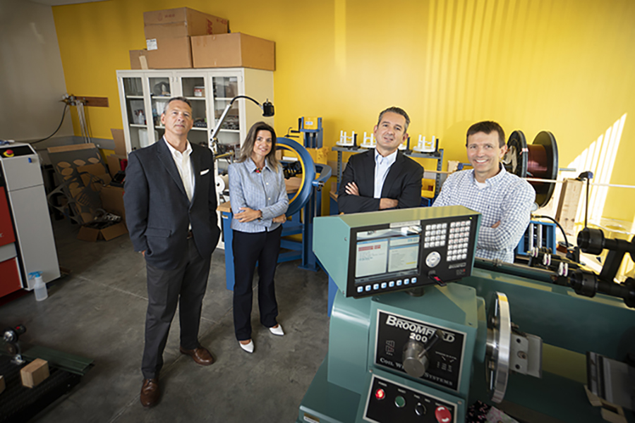 Purdue University engineers, from left, John Haddock, Nadia Gkritza, Dionysios Aliprantis and Steve Pekarek stand in the lab where they are testing technology they designed to enable electric vehicles to receive power from the road. There are several large instruments that surround them in the lab.