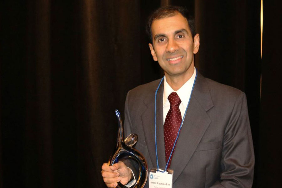 A well-dressed man stands with an award in hand, symbolizing success and recognition in his field