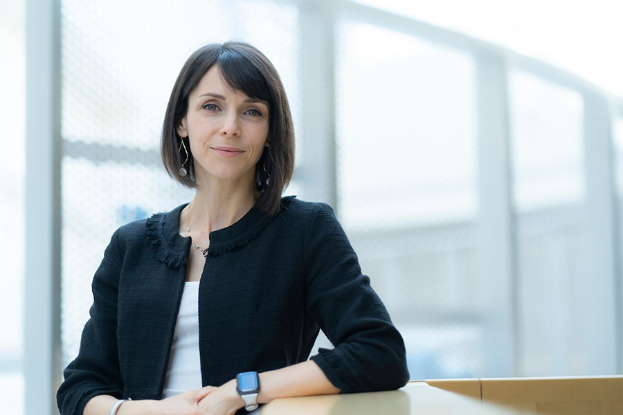 A professional woman in a business suit posing with her elbow on a wooden railing looking at the camera