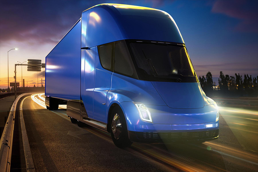 A Tesla semi truck driving on a dark road at night, illuminated by streetlights and the truck's headlights