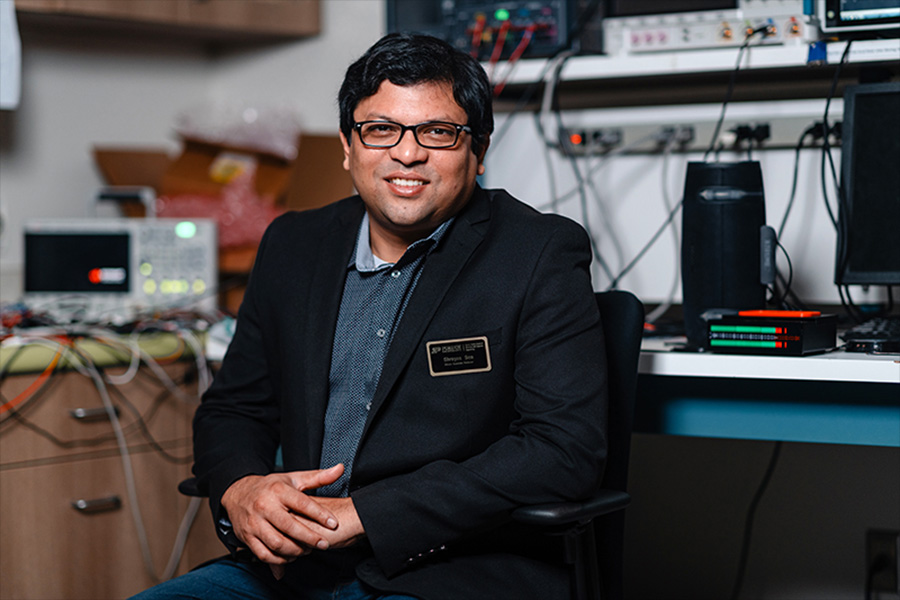 A man wearing glasses is seated at a desk in his lab, looking forward, posing for a photo..