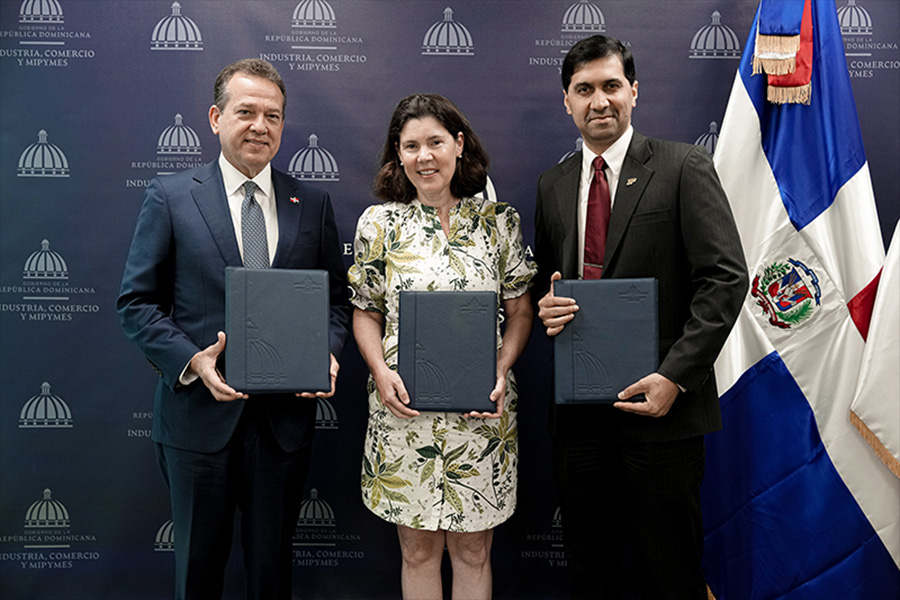 Group of three people standing together, each holding documents in front of a flag.