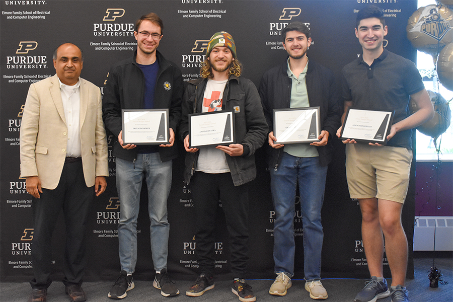 4 students pose for a photo with Professor Thottethodi. They are standing in front of the ECE branded step and repeat.