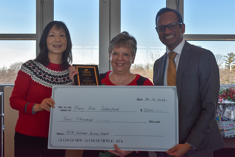 Dan Jaio, Mary Ann Satterfield, and Milind Kulkarni pose for a photograph at the staff recognition luncheon. Mary Ann is holding a plaque while Dan and Milind present a large check.