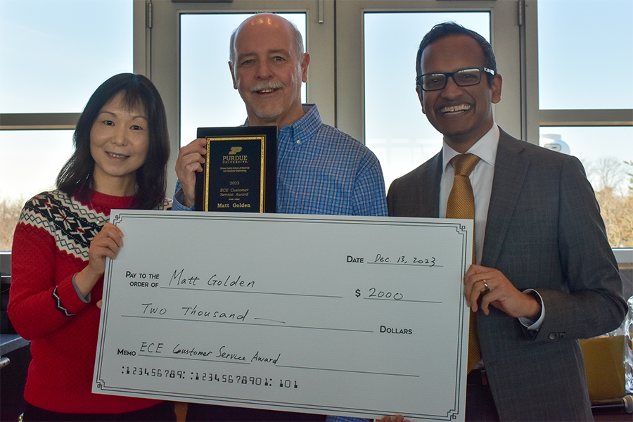 Dan Jiao, Matt Golden, and Milind Kulkarni pose for a photograph at the staff recognition luncheon. Matt is holding a plaque while Dan and Milind present a large check.