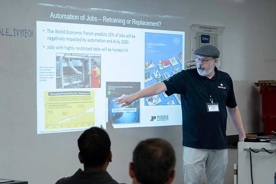 A man is seen giving a presentation, standing before a screen that showcases important visuals and data