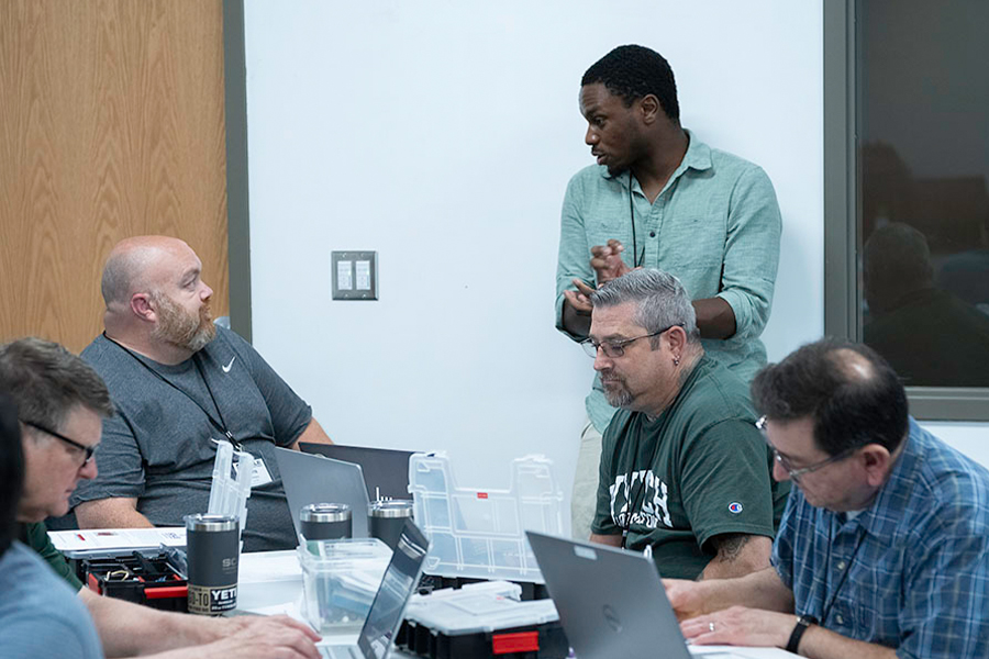A diverse group of individuals engaged in discussion while working on laptops around a conference table