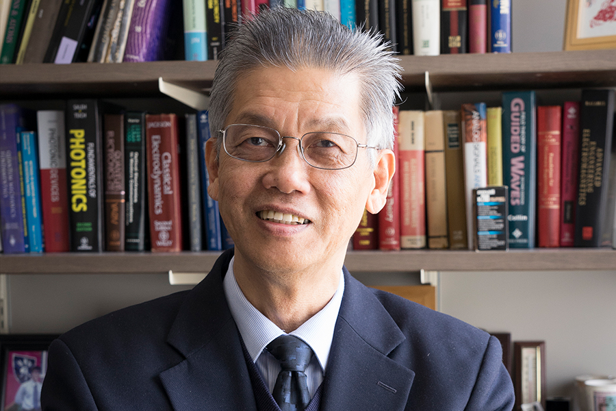An Asian professional in a suit and tie, standing in front of a bookshelf