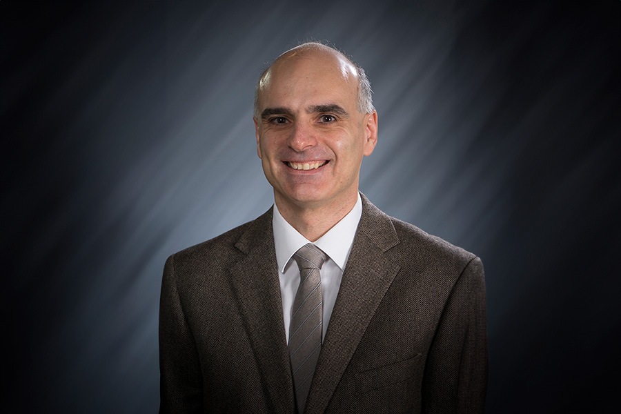 Dimitrios Peroulis poses for a portrait. He is wearing a dark suit, white shirt, and dark tie.