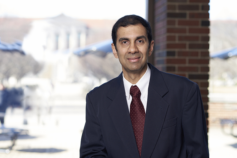 Professor Anand Raghunathan poses for a photo in the atrium of the MSEE building. He is wearing a white shirt, red tie, and dark suit.