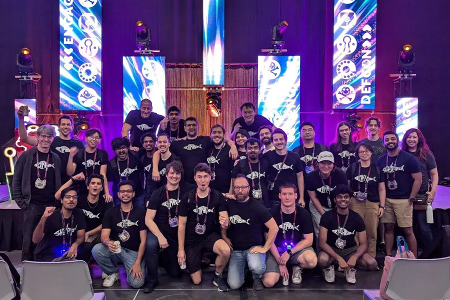 A diverse group of individuals smiling and posing together for a photograph on a stage, showcasing camaraderie and celebration