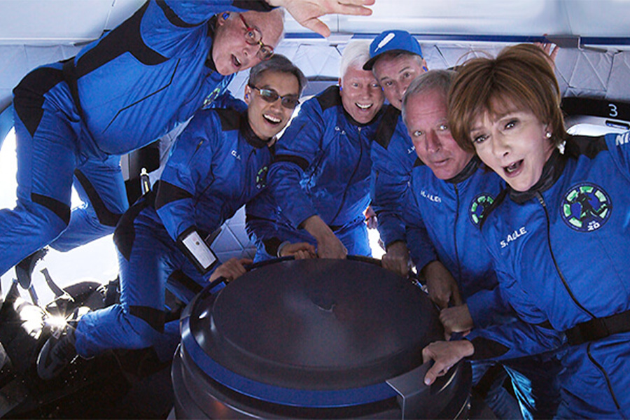 A diverse group of individuals wearing blue spacesuits posing inside the Blue Origin rocket, New Shepard