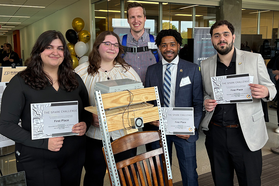 Five individuals proudly display certificates while standing behind a chair.