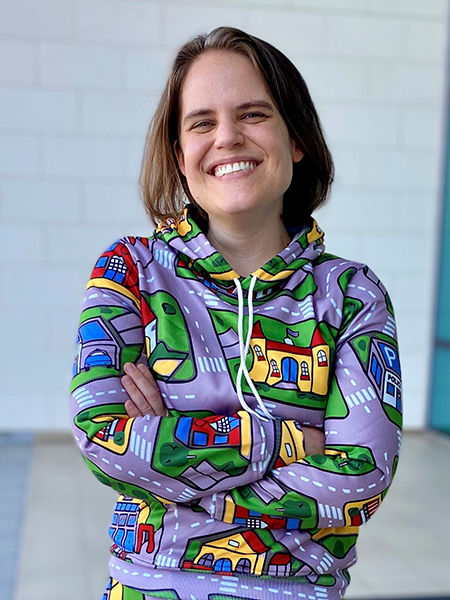 Woman with brown hair, smiling, wearing colorful, patterned hoodie