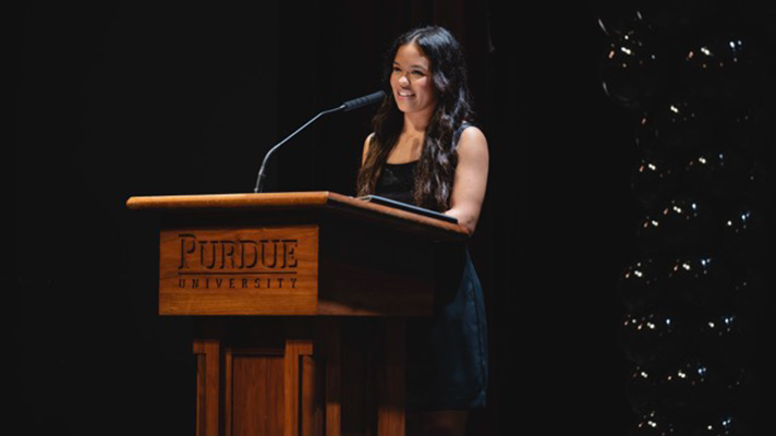 Female student with long dark hair, standing behind lectern