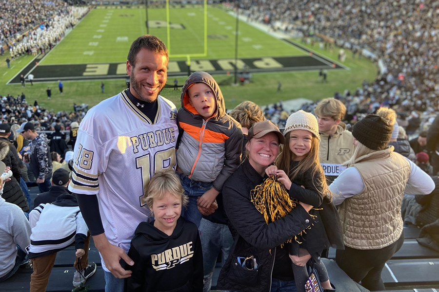 Man, woman and three kids wearing Purdue gear in the stands at a Purdue football game